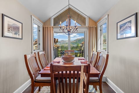 A spacious dining room with a long wooden table and chairs, offering a panoramic view of the mountains.