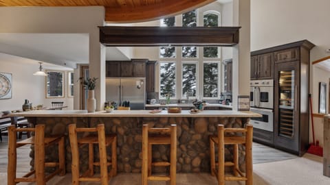 Spacious kitchen with a stone-front breakfast bar, vaulted ceilings, and forest-facing windows.