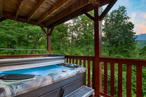 Covered deck with a private hot tub and forest views.