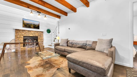 Open concept living room with stone fireplace, TV, and leather couch.