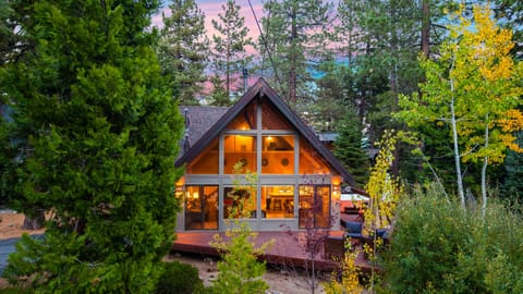 Classic A-frame cabin exterior with glowing windows framed by towering pines.