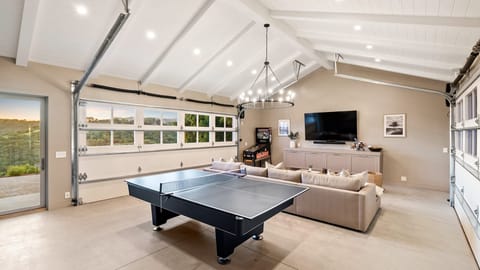 The game room features a sectional couch, a ping pong table, TV and an arcade game. (View House)