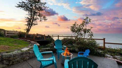 Oceanfront patio with chairs and firepit at sunset.