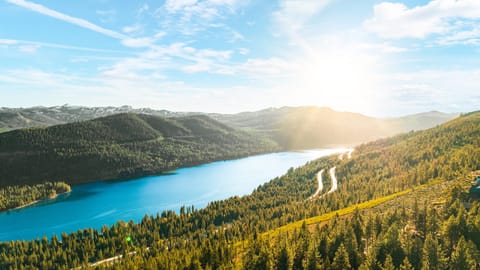 Daytime aerial of nearby lake and winding forest road.
