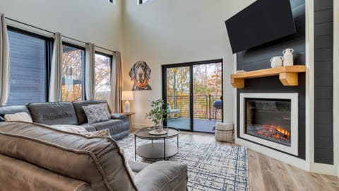 Modern living room featuring a high ceiling, multiple windows, a TV, and a fireplace.
