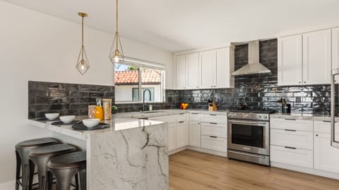 Sleek modern kitchen with marble waterfall island, stainless steel appliances, and chic black tile backsplash—perfect for gathering and entertaining.