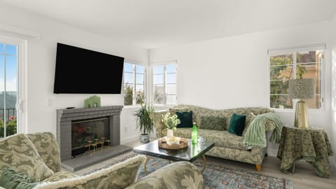 Main living area with plush, textured green sofas, a fireplace, and large windows offering scenic views.
