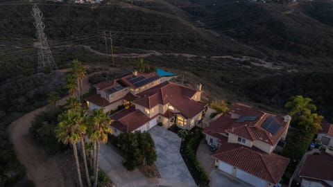 Aerial view of the large Mediterranean-style home and surrounding hilly landscape at sunset/dusk.
