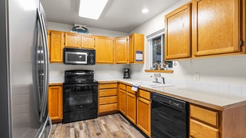 Kitchen with light wood cabinets, black appliances, and wood-look flooring.