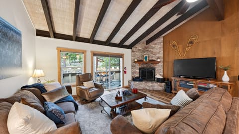 Cozy cabin living room with vaulted ceilings, fireplace, and deck access.