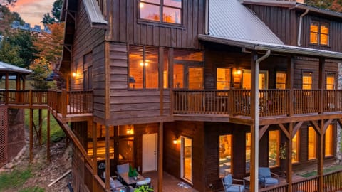 Warm mountain retreat with multiple covered decks, glowing interiors, and cozy cabin charm at sunset.