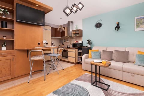 An open view of the living space with a wall-mounted TV, wooden cabinetry, and bar stools, providing a functional and stylish setup.

