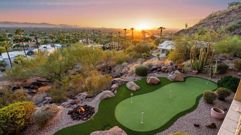 Elegant backyard with a putting green, fire pit, and city views at sunset.