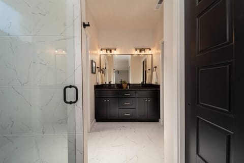 Spacious and luxurious bathroom featuring marble flooring, a large glass shower, and a dual vanity set against a rich, dark cabinetry