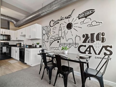 Modern kitchen and dining space with bold Cleveland mural art on display   - Black dining table with four chairs ideal for meals or working remotely   - White cabinets, black countertops, and subway tile create a fresh modern look