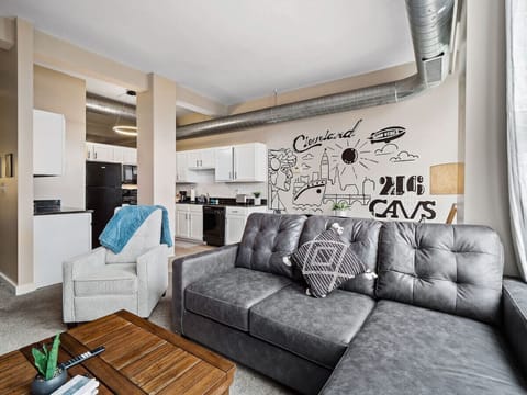 Stylish living space with sectional sofa, accent chair, and wood coffee table   - Large wall mural showcasing Cleveland pride with modern artistic design   - Open layout connects seamlessly with kitchen and dining area for comfort