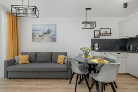 A modern open-plan living and dining area featuring a gray sofa, a round dining table, and a sleek black kitchen, accented with yellow decor elements.

