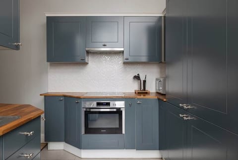 A modern kitchen with navy-blue cabinets, wooden countertops, and stainless steel appliances, offering a sleek and functional cooking space.

