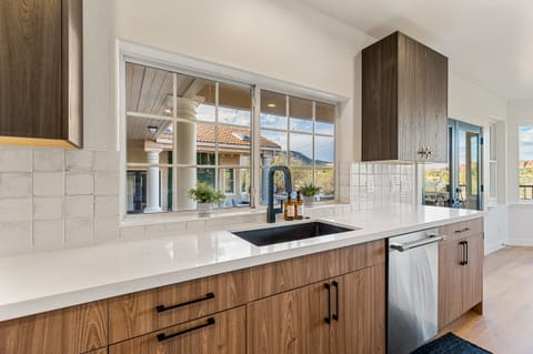 - Sedona kitchen counter with modern sink and bright window views - Warm wood cabinetry pairs with sleek white surfaces - Scenic outdoor patio visible through large windows