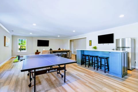 Enjoy the ultimate entertainment and relaxation hub with a marble island, ping pong table, 4K smart TV, and cozy couch in this inviting room.