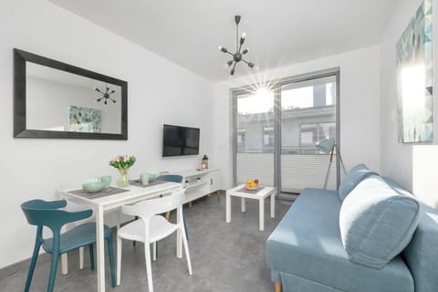 A bright and stylish space with a modern blue sofa, a dining table with chairs, and a TV.