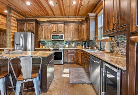 The wide angle of the kitchen reveals a spacious area with dark wooden cabinets, a stacked stone backsplash, and bar seating.