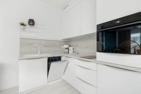A compact but functional kitchen with glossy white cabinetry and a modern black backsplash.

