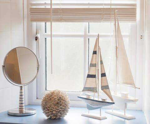 Window sill in bathroom with shaving mirror, sail boat ornaments, blind