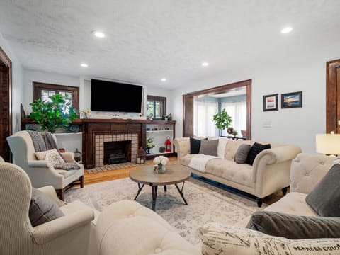 Relax in this bright living room featuring tufted sofas, a stylish coffee table, hardwood floors under a plush area rug, and a classic wood-burning fireplace—perfect for cozy evenings or social gatherings! 🛋️🔥🕯️