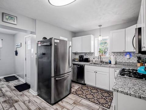 Bright, modern kitchen with crisp white cabinets, granite countertops, and subway tile backsplash. Stainless appliances and patterned wood-look floors flow seamlessly into the adjacent dining room for effortless entertaining! 🍽️✨🏡