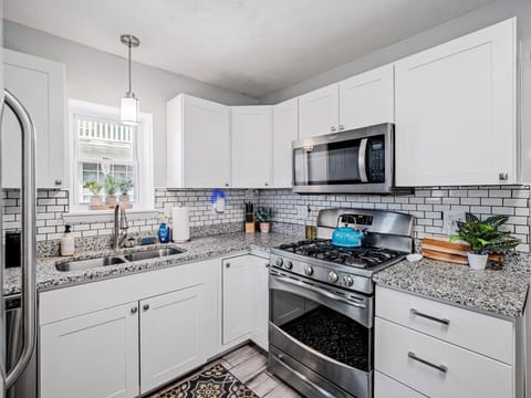 Bright, modern kitchen with crisp white cabinets, granite countertops, and subway tile backsplash. Stainless appliances and patterned wood-look floors flow seamlessly into the adjacent dining room for effortless entertaining! 🍽️✨🏡