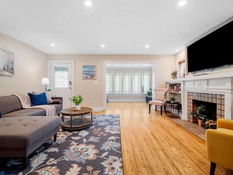 Bright and cozy living room with a comfy sectional 🛋️, floral rug 🌸, and a charming fireplace 🔥. Open layout flows into a stylish dining area — perfect for relaxing or entertaining 🍷✨.