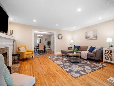 Bright and cozy living room with a comfy sectional 🛋️, floral rug 🌸, and a charming fireplace 🔥. Open layout flows into a stylish dining area — perfect for relaxing or entertaining 🍷✨.