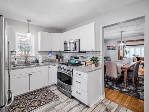 Bright, modern kitchen with crisp white cabinets, granite countertops, and subway tile backsplash. Stainless appliances and patterned wood-look floors flow seamlessly into the adjacent dining room for effortless entertaining! 🍽️✨🏡