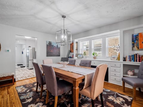 Gather around this spacious dining area featuring a solid wood table for six, elegant chandelier lighting, cozy upholstered chairs, and built-in storage under bay windows—ideal for family meals or game nights! 🍽️💡🎲🌿