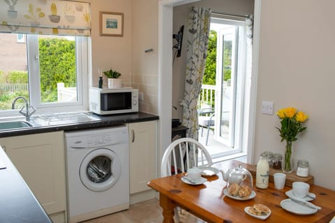 open kitchen with dining table, washing machine, microwave with plant on top and sink under window