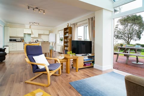 Living area with patio doors to outside deck, tv, kitchen and dining table