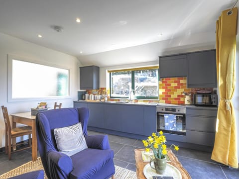 Kitchen area on one side with chair, coffee table, vase of flowers on the other side