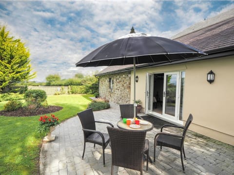 Patio area with table, four chairs and parasol leading to the garden
