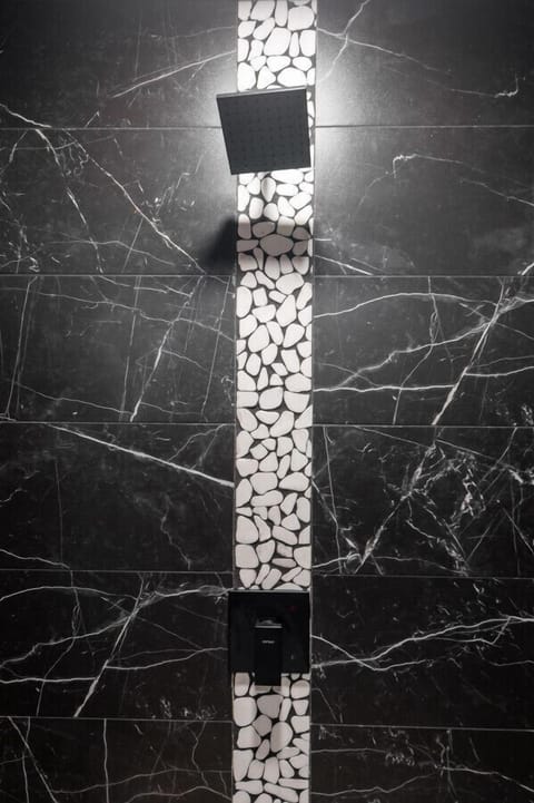 Luxurious black marble shower with pebble accents, rainfall showerhead, and modern design!