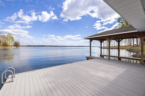 A spacious wooden dock extends over calm lake waters under a vast sky with fluffy clouds, offering a peaceful setting