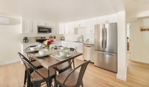 - Bright kitchen with stainless steel fridge and oven  
- Dining table set for family meals with modern style  
- White cabinets provide storage and sleek clean look  