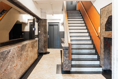 An architectural blend of modern and traditional design elements in a building’s interior, featuring marble stairs with contrasting metal handrails that lead through various multi-textured levels, creating a dynamic and visually appealing space.