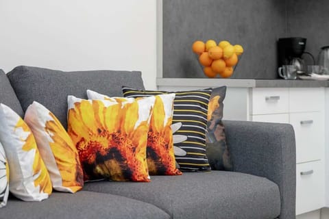 A grey sofa with bright orange pillows and a flower painting above it. The space is cozy, with a modern and cheerful vibe.