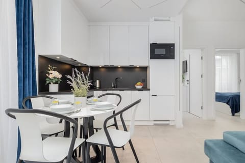 Dining Area & Kitchen – Dining area with a round table, turquoise sofa in the background, and a bright modern kitchen.

