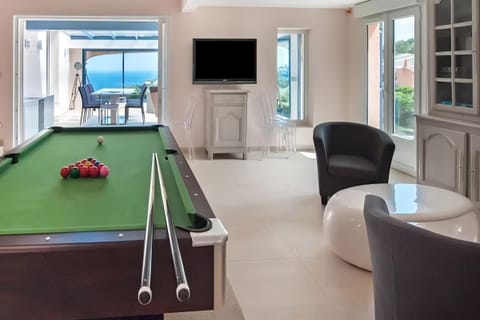 This spacious game room features a full-size billiard table, perfect for entertaining guests or enjoying a friendly competition.  The room is bathed in natural light from the large windows, offering views of the surrounding landscape. The room is also equ