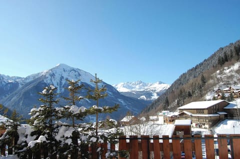 Enjoy breathtaking views of the snow-capped French Alps from the chalet's balcony.  The view features a picturesque village nestled amidst the mountains and a clear blue sky, creating a serene and inspiring atmosphere.