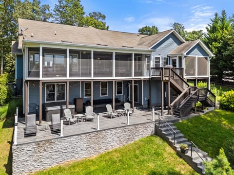 A stunning lakefront home with a spacious screened porch, surrounded by a lush green lawn and a charming stone pathway leading down to the water.