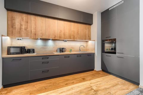 Modern kitchen area with grey cabinets, wooden countertops, and bright lighting.
