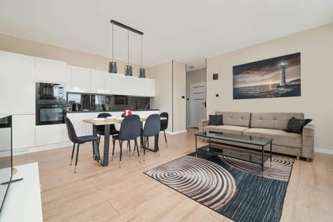 Modern and spacious living room with a sofa, TV and kitchenette with dining table and chairs.